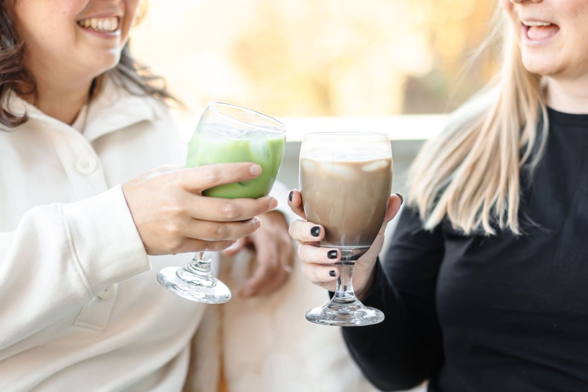 A brunette woman holding a matcha latte and a blonde woman holding a hojicha latte both made by Matcha Nude